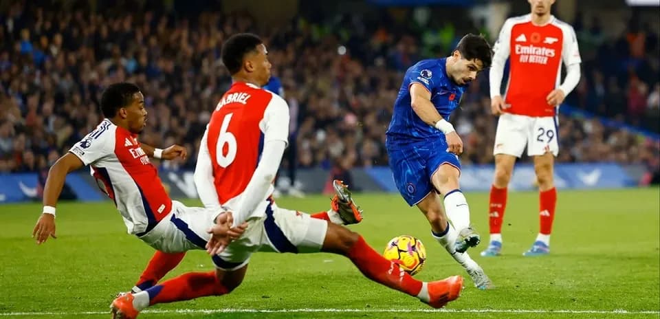Chelsea player shooting while Arsenal defenders attempt tackle