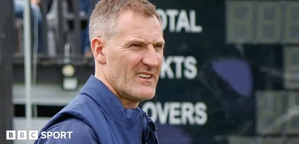 Coach observing match with scoreboard in background