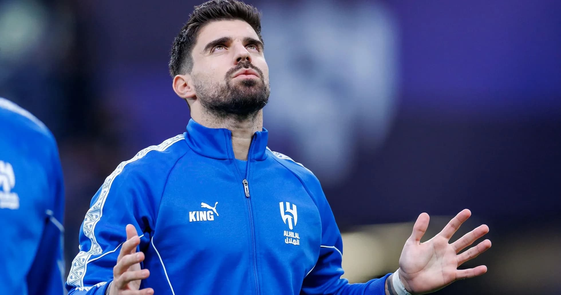 Player in blue tracksuit looking up before match