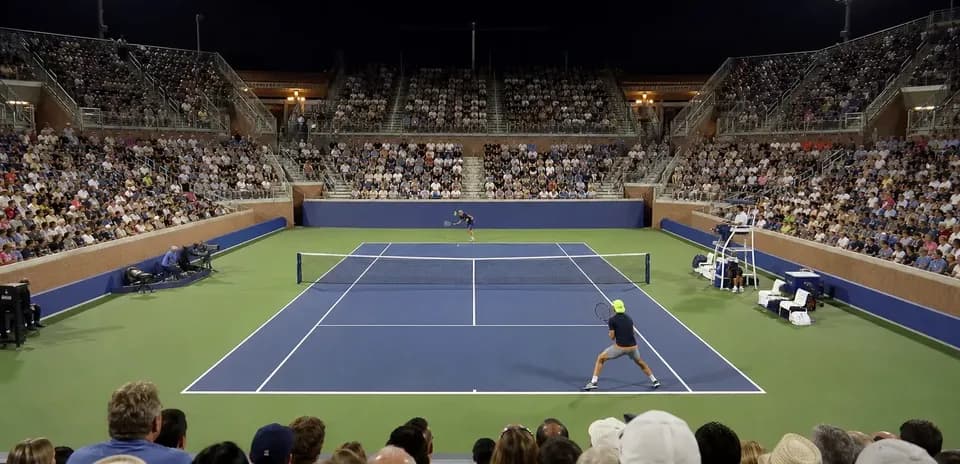 Players competing in a night tennis match with spectators