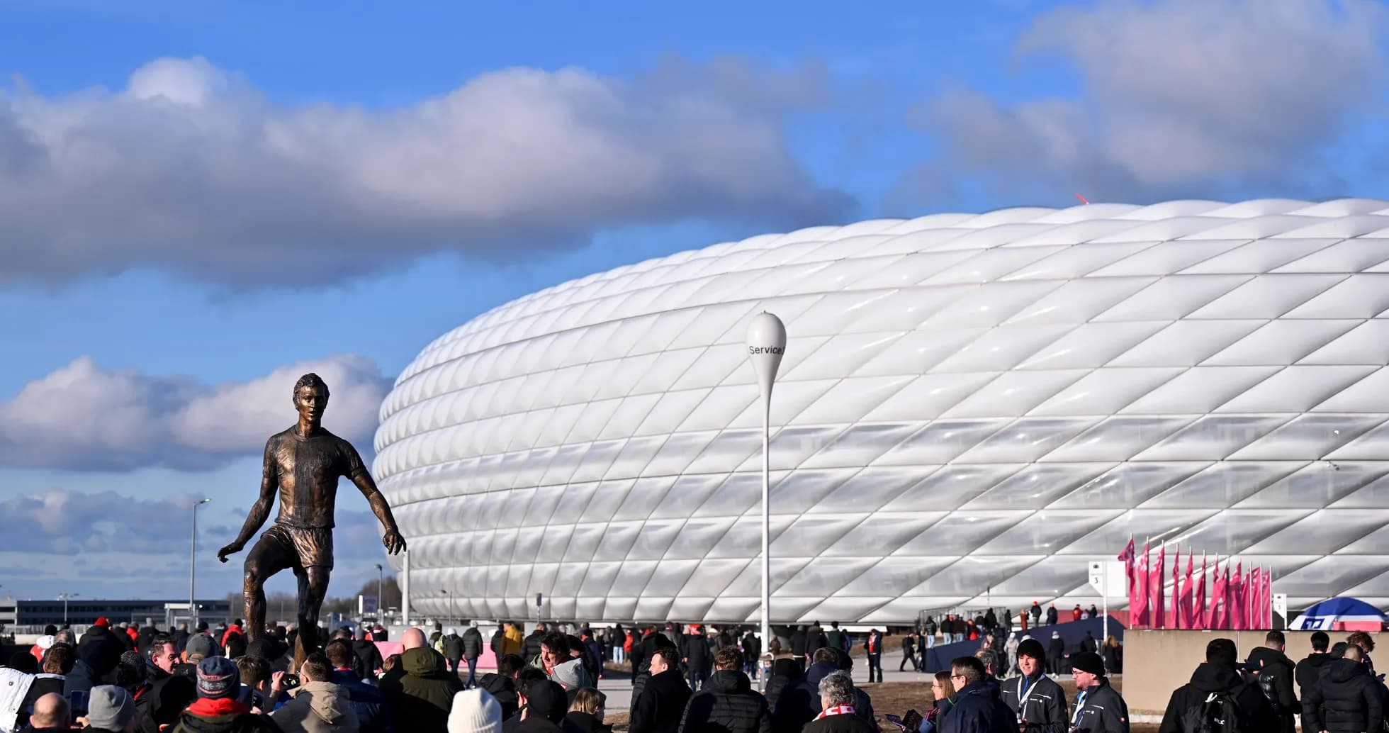 Fans gathering near stadium with statue in foreground
