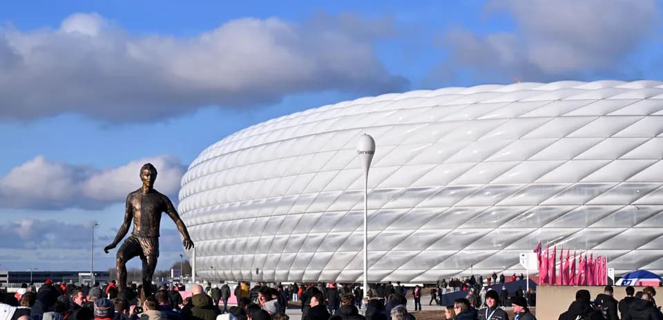 Fans gathering near stadium with statue in foreground