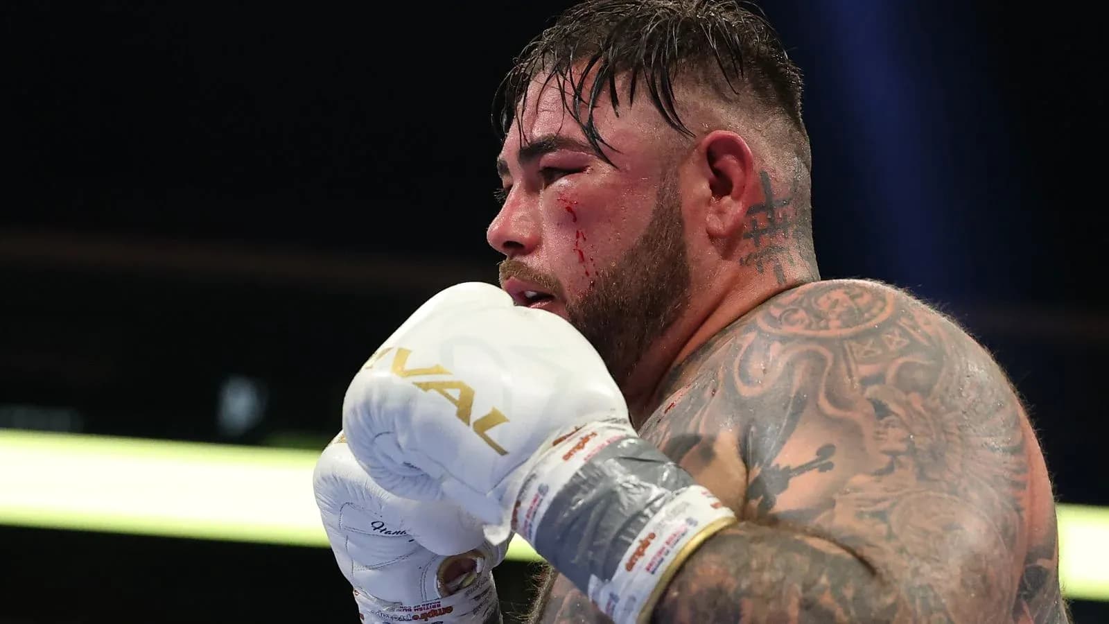 Boxer with tattoos and blood on face during match