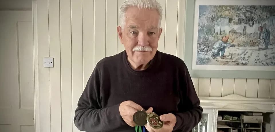 Elderly man holding medals in indoor setting