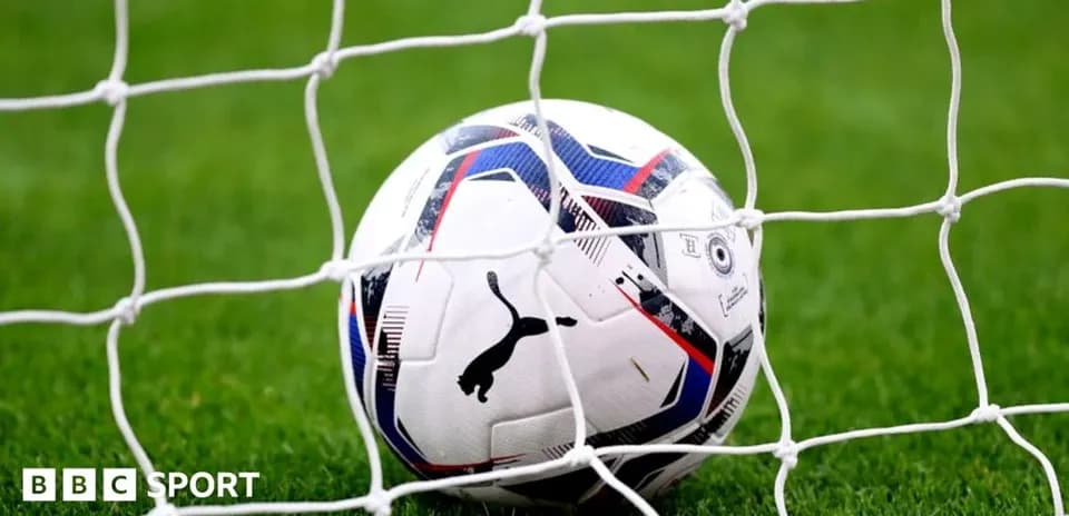 Football in goal net on grassy field