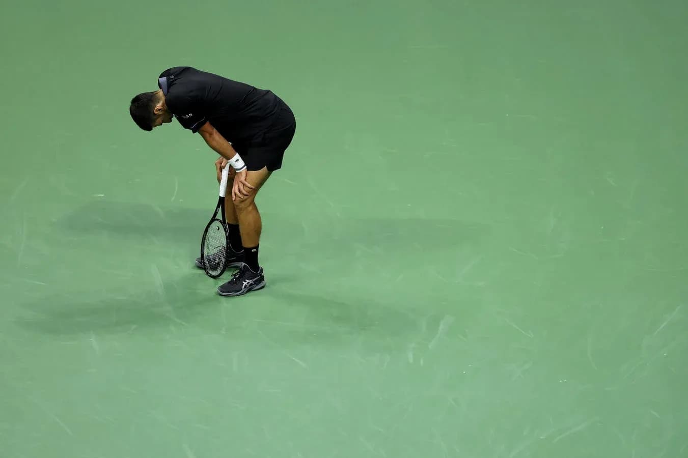 Tennis player bending over on court with racket