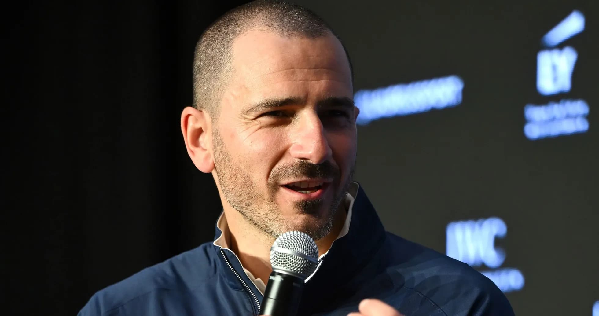 Man speaking into a microphone at an event Man speaking into a microphone at an event