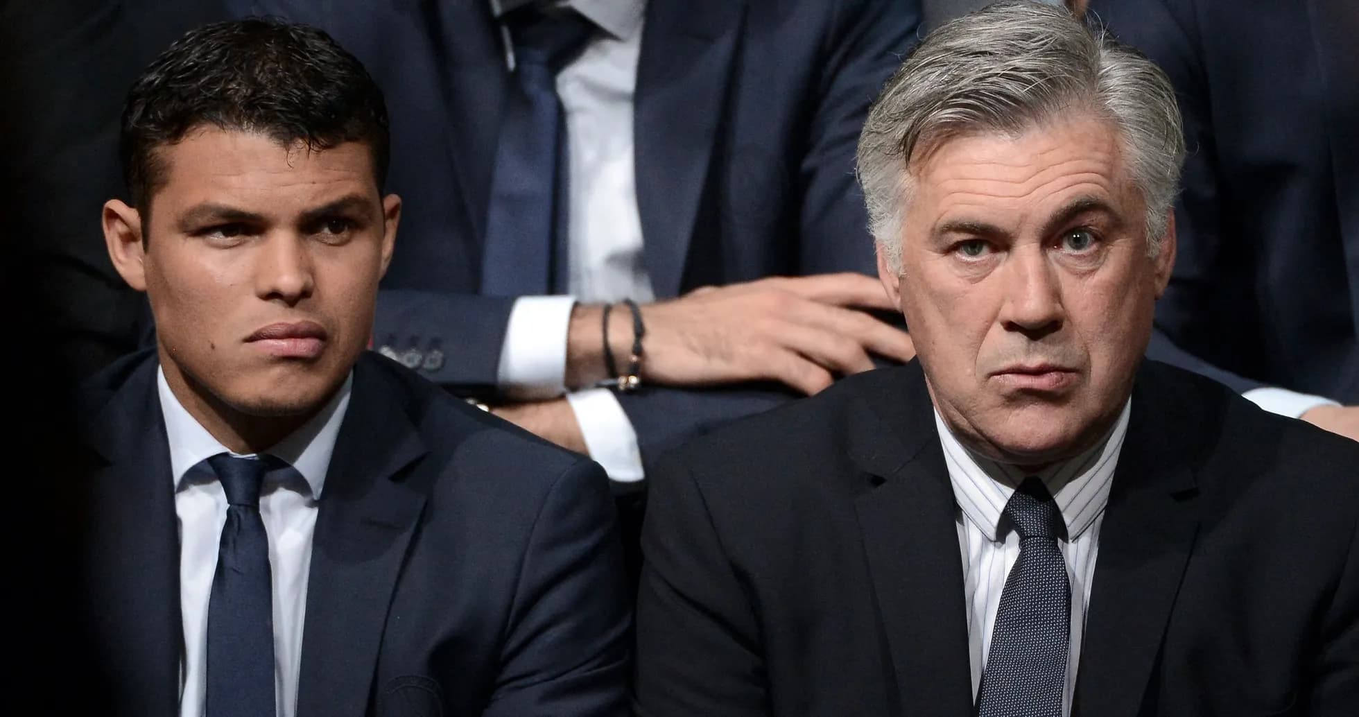 Two men in suits sitting together at event Two men in suits sitting together at event