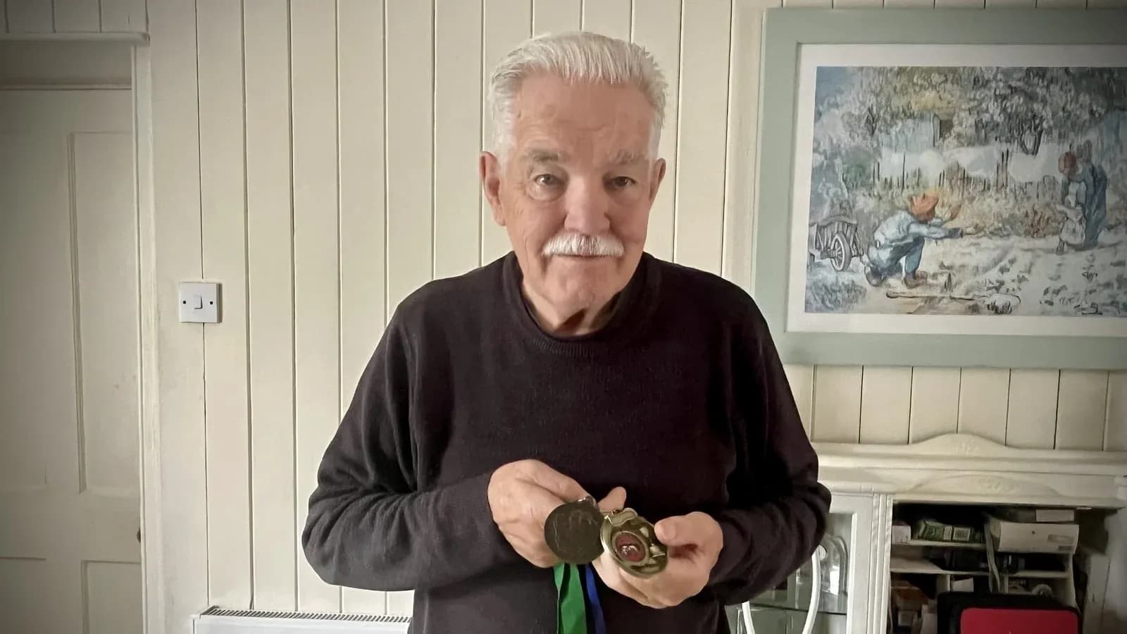 Elderly man holding medals in indoor setting Elderly man holding medals in indoor setting