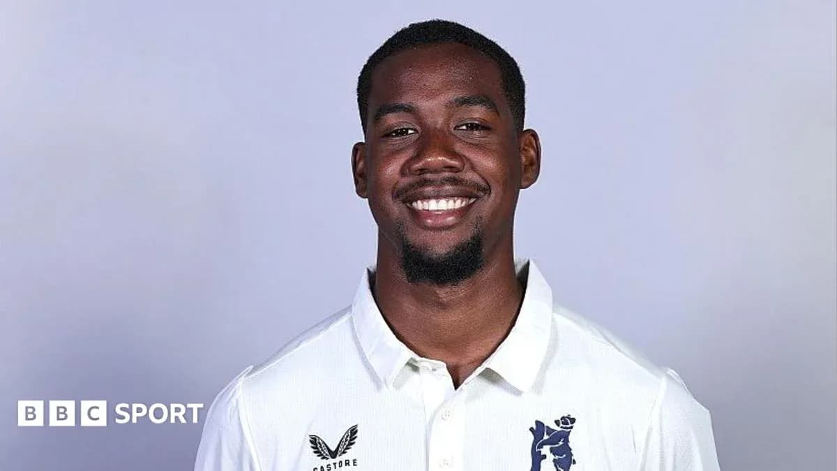 Cricketer smiling in team uniform against plain background Cricketer smiling in team uniform against plain background